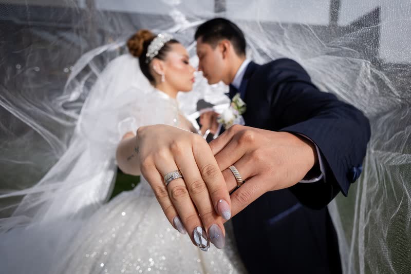 Detalle de las manos de los novios mostrando los anillos sobre el velo