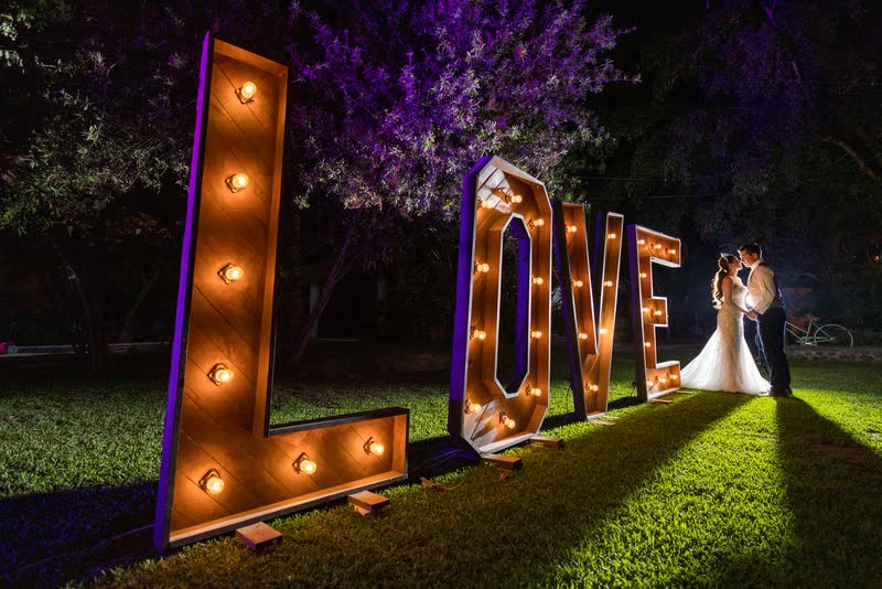 Novios de noche junto a letras gigantes iluminadas que forman la palabra LOVE