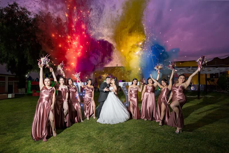 Novia con sus damas lanzando polvos de colores al aire en el jardín