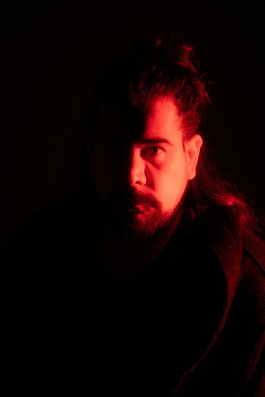 Retrato de un hombre de barba bajo luz roja con sombras profundas