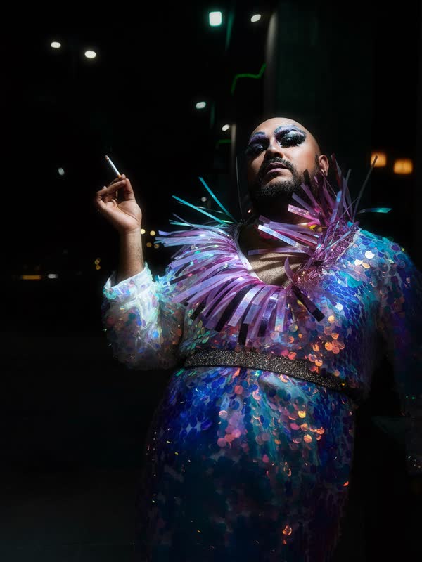 Artista con vestuario de lentejuelas iridiscentes y maquillaje brillante, de noche en la calle