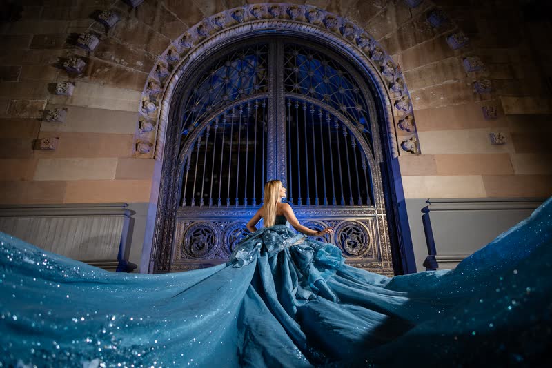 Vestido azul con cauda frente a una reja monumental iluminada en la oscuridad