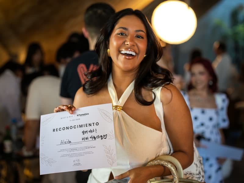 Asistente sonriendo con su reconocimiento en un evento corporativo