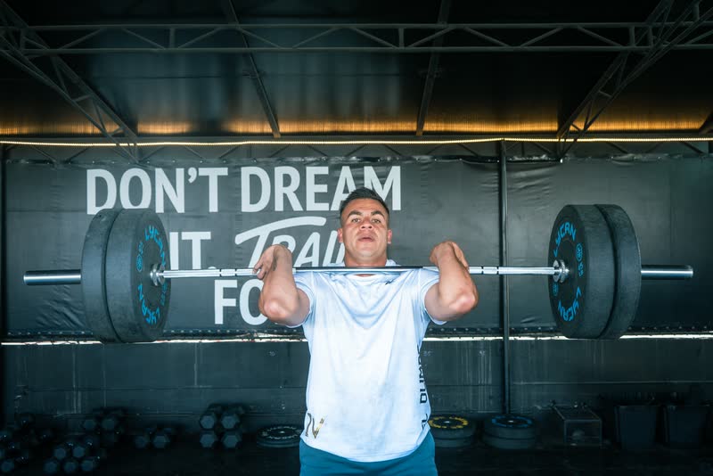 Atleta con la barra al hombro frente al lema Don't dream it, train for it