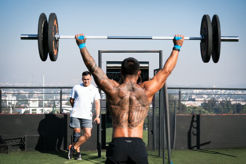 Atleta tatuado de espaldas en una barra de dominadas en la azotea