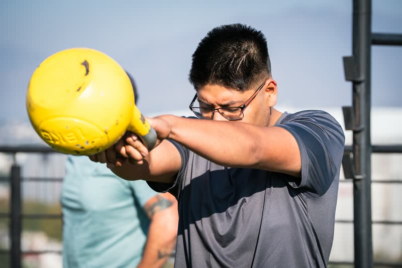 Hombre levantando una kettlebell amarilla al aire libre