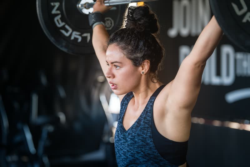 Mujer haciendo press de hombros con barra en el gimnasio