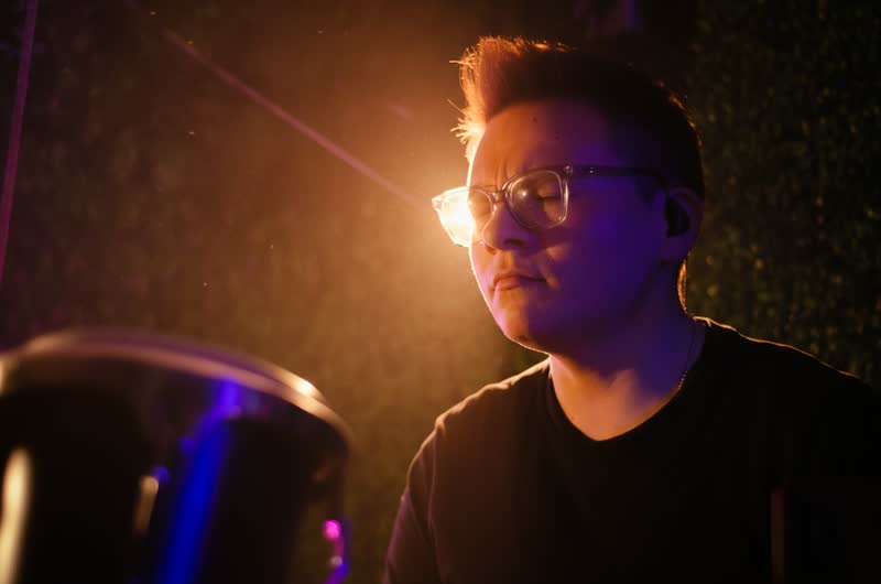 Productor con lentes frente a su equipo, luz naranja y violeta