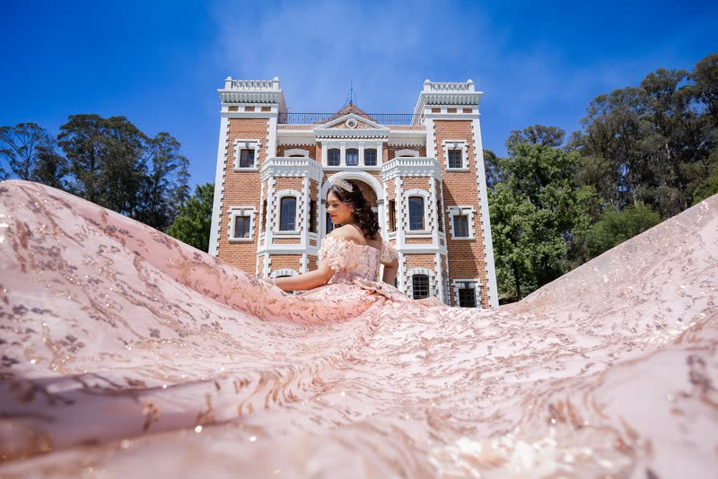 Quinceañera con vestido rosa frente a una hacienda amarilla